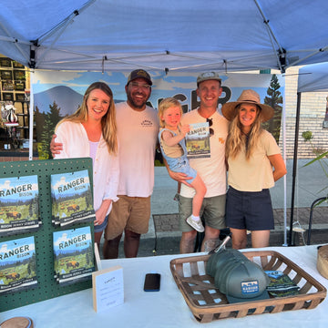 Family of four standing under a blue tent with promotional materials and a basket on a table.